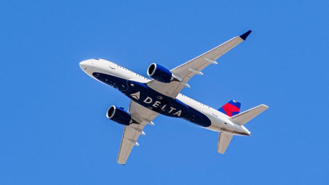 Delta Airlines aircraft in flight, with logo on the plane's underbelly; blue sky background