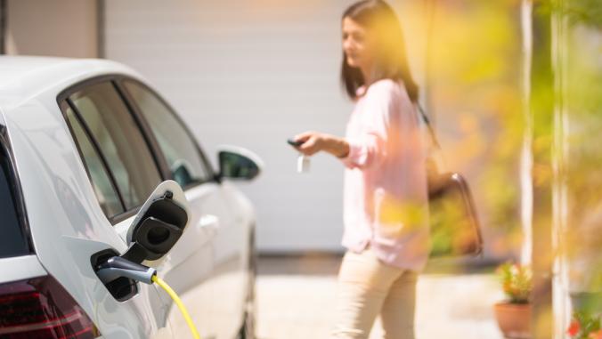 Close up of a electric car charger with person in the background, locking a car