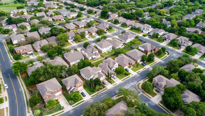 An aerial shot of a suburban neighborhood, with green lawns and lush trees.
