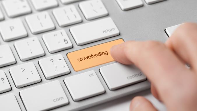 A picture of a keyboard with a finger pressing an orange key with the word 'crowdfunding' on it